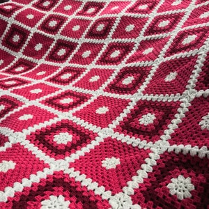 Könnte beinhalten: Eine gehäkelte Decke mit einem geometrischen Muster in Rosa- und Weißtönen.