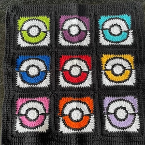 May include: A black crochet blanket with nine squares featuring different colored Pokeball designs. Each square has a white outline and a white circle in the center. The colors of the Pokeballs are green, purple, blue, red, yellow, pink, orange, and lavender.