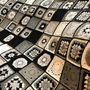 May include: A black and white crochet blanket featuring a range of different patterns. The blanket is composed of squares with various designs, including flowers, stars, and geometric shapes.