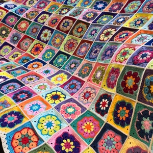 May include: A colourful crocheted blanket featuring a variety of flower designs in shades of pink, purple, blue, green, yellow and orange.