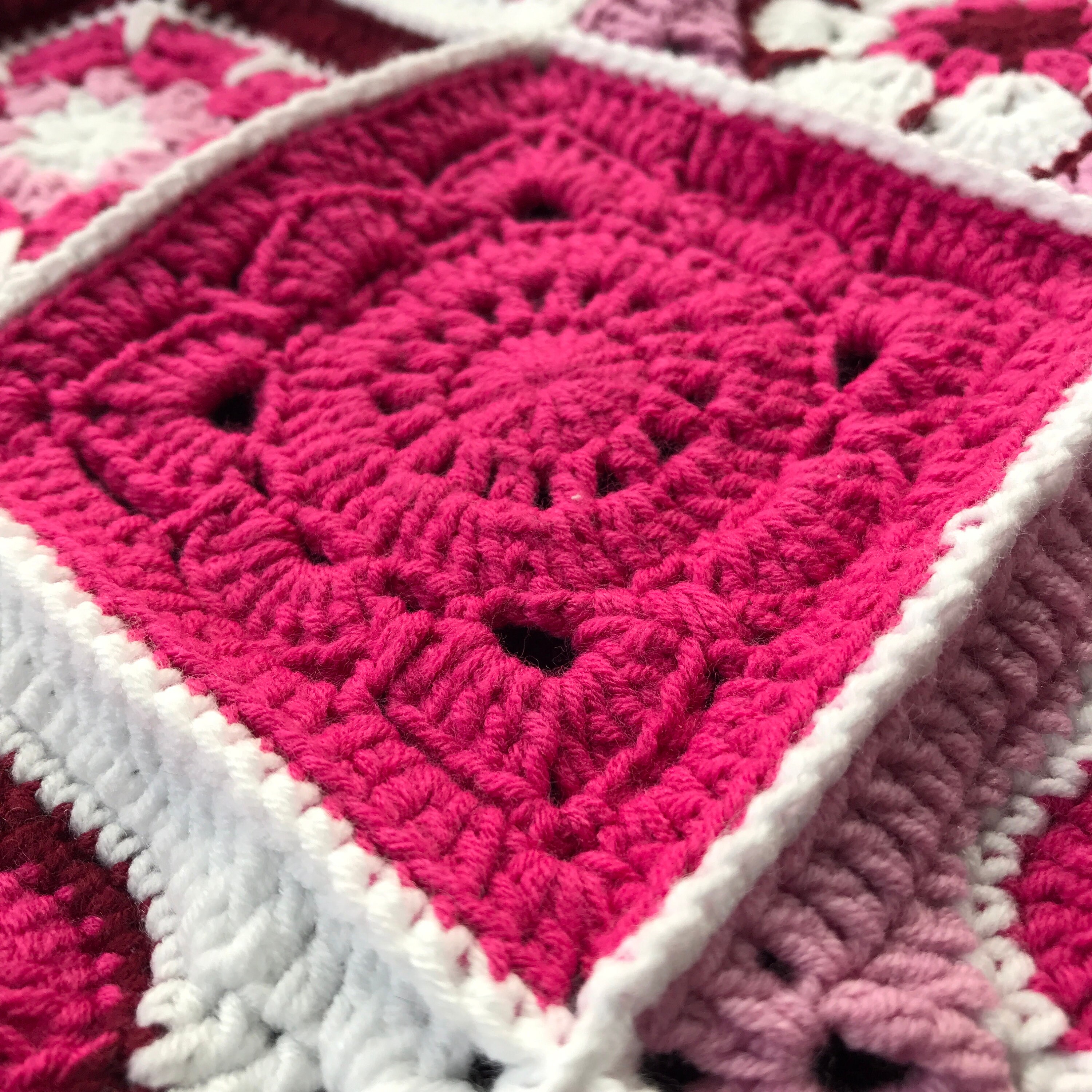 ピンク、バーガンディ、ホワイトの花柄かぎ針編みブランケット。自分