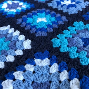 Può includere: Primo piano di una coperta all'uncinetto con un motivo ripetitivo di quadrati blu, bianchi e blu scuro.