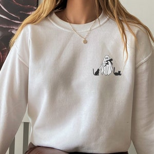 May include: White sweatshirt with a black and white graphic of a ghost holding two cats. The ghost is wearing a scarf.