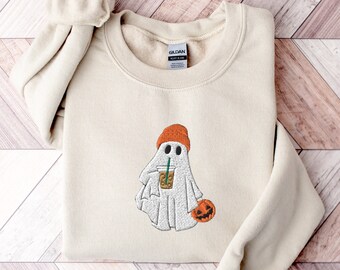 May include: A beige sweatshirt with an embroidered design of a ghost wearing an orange beanie and holding a cup of coffee. The ghost is holding a small orange pumpkin.