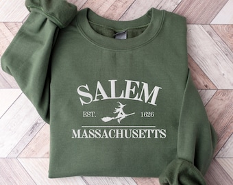 May include: A green sweatshirt with a white graphic print that says "SALEM EST. 1628 MASSACHUSETTS" with a witch flying on a broomstick in between the words "EST." and "1628".