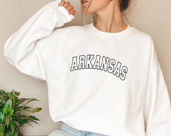 Può includere: Felpa bianca con testo nero che recita "ARKANSAS" in un font universitario.