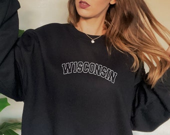 May include: Black sweatshirt with a white outline of the word "WISCONSIN" in an arched font.