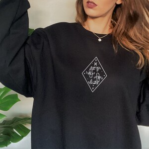 Puede incluir: Sudadera negra con un gr&aacute;fico blanco del s&iacute;mbolo del zod&iacute;aco Piscis en forma de diamante.