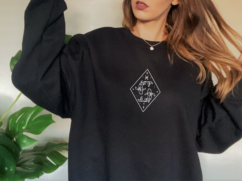 Puede incluir: Sudadera negra con un gr&aacute;fico blanco del s&iacute;mbolo del zod&iacute;aco Piscis en forma de diamante.