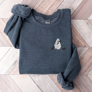 May include: A dark blue sweatshirt with a white ghost holding a cat on the front. The ghost is surrounded by two black cats.