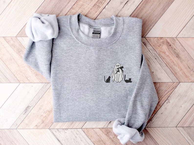 May include: A gray sweatshirt with a ghost holding a cat and two other cats sitting on the ground. The ghost and cats are black.