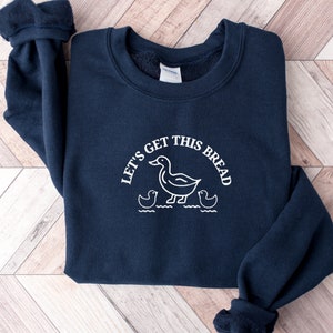 May include: A navy blue sweatshirt with a white graphic of ducks and the text "Let's get this bread".