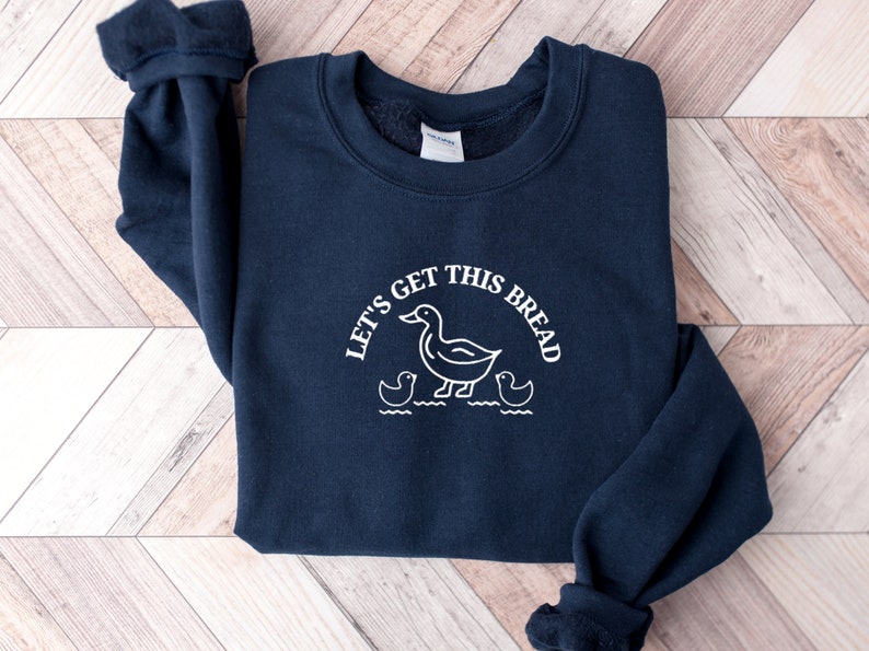 May include: A navy blue sweatshirt with a white graphic of ducks and the text "Let's get this bread".