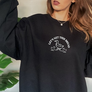 May include: Black sweatshirt with a white embroidered design of a duck and ducklings with the text "Let's get this bread".