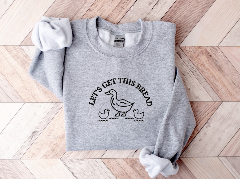 May include: Gray sweatshirt with a black graphic of a duck and the text "Let's get this bread".