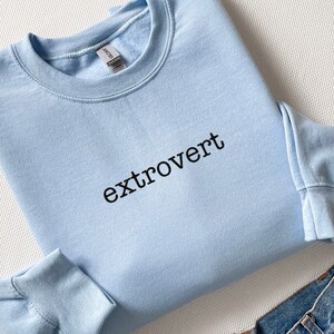 Op de afbeelding: Een lichtblauw sweatshirt met het woord "extrovert" in het zwart op de voorkant.
