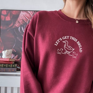 May include: Burgundy sweatshirt with a white graphic of a duck and ducklings with the text "Let's get this bread".