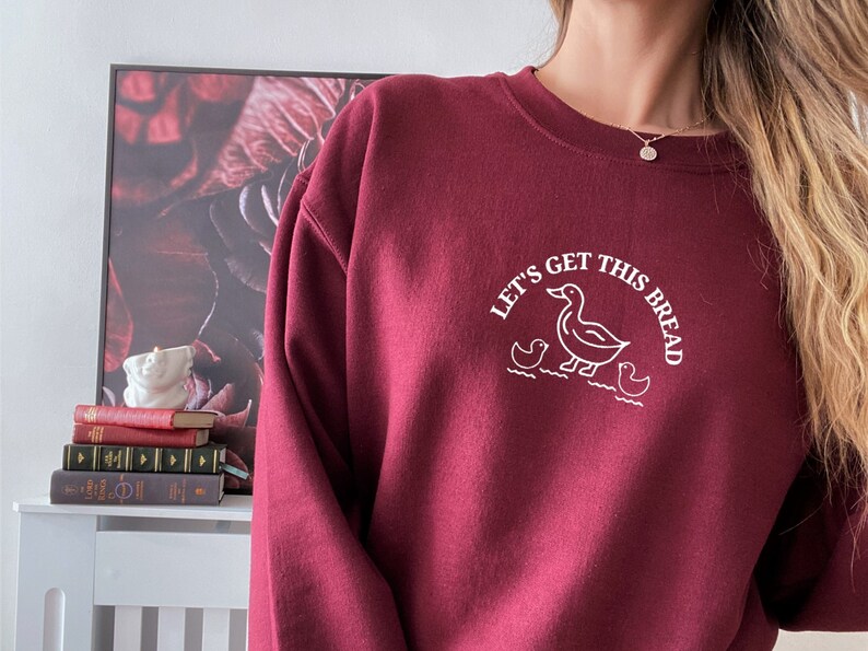 May include: Burgundy sweatshirt with a white graphic of a duck and ducklings with the text "Let's get this bread".