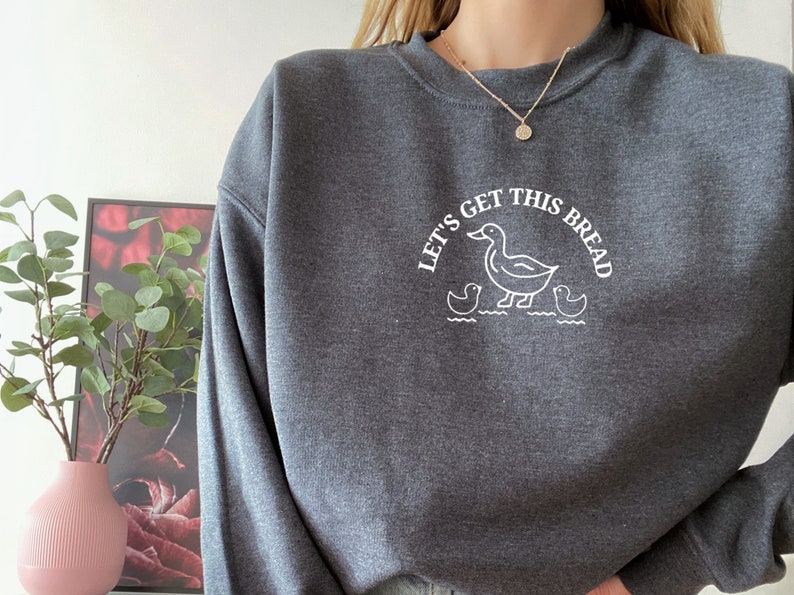 May include: A dark gray sweatshirt with a white graphic of ducks and the text "Let's Get This Bread".