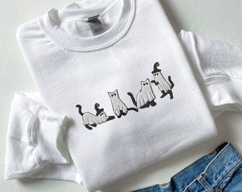 Puede incluir: Sudadera blanca con un diseño bordado de cinco gatos disfrazados de fantasmas para Halloween.