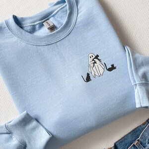 May include: A light blue sweatshirt with a white ghost holding a black cat and three black cats walking behind it.