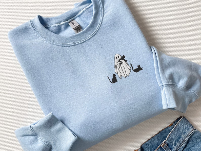 May include: A light blue sweatshirt with a white ghost holding a black cat and three black cats walking behind it.