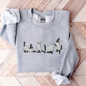May include: A gray sweatshirt with a design of five cats dressed as ghosts for Halloween. The cats are in a line, with one cat wearing a witch's hat.