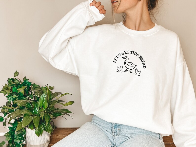 May include: White sweatshirt with a black graphic of a duck and the text "Let's Get This Bread".