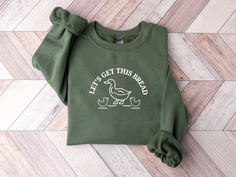 May include: A green sweatshirt with a white graphic of ducks and the text "Let's get this bread".