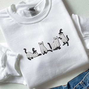 May include: White sweatshirt with an embroidered design of five cats dressed as ghosts for Halloween.