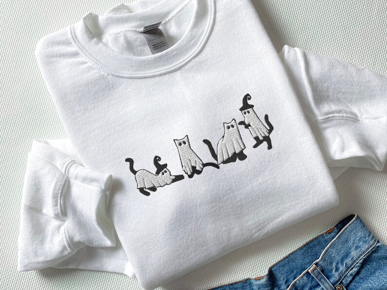 May include: White sweatshirt with an embroidered design of five cats dressed as ghosts for Halloween.