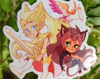 May include: A glossy sticker featuring two cartoon characters from the animated series She-Ra and the Princesses of Power. One character is blonde and holds a sword, the other has brown hair and cat ears. A unicorn and a winged creature are also depicted.