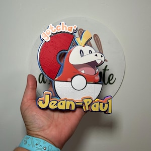 May include: A colorful, layered decoration featuring a cartoon character inside a red and white ball. The character is red, white, and yellow. The text "gotcha" and "Jean-Paul" are also visible.