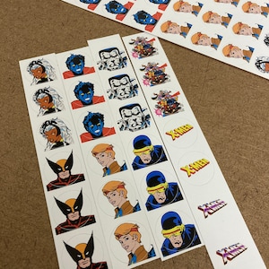 Puede incluir: Un conjunto de pegatinas redondas con varios personajes de la serie de cómics X-Men. Las pegatinas presentan personajes como Lobezno, Cíclope, Tormenta y Bestia. Las pegatinas están impresas en papel blanco con un acabado brillante.