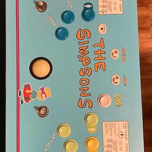 May include: A blue and yellow arcade cabinet with The Simpsons characters and buttons for playing the game. The cabinet has a control panel with buttons for attack and jump, as well as a joystick. The cabinet also has a volume knob and an on/off switch.