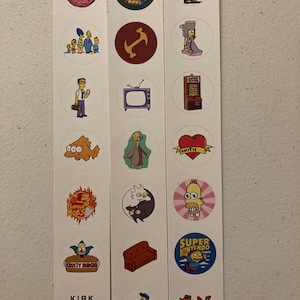 Puede incluir: Una hoja de pegatinas con varios personajes y logotipos de dibujos animados. Los diseños incluyen una rosquilla, la familia Simpson, un televisor, un sofá y el logotipo de Flaming Moe's. Las pegatinas son redondas y coloridas.