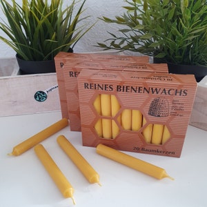 Puede incluir: Una caja de 20 velas de cera de abeja pura, etiquetada "REINES BIENENWACHS" con un patrón de panal y una ilustración de colmena. Las velas son amarillas y están dispuestas en una caja con un fondo marrón. El texto "20 Baumkerzen" está impreso en la parte inferior de la caja.