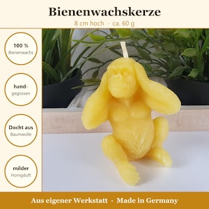 May include: A yellow beeswax candle shaped like a gorilla covering its ears with its hands. The candle features a cotton wick at the top of the head. Text on the image includes Bienenwachskerze, 8 cm hoch, ca. 60 g, 100% Bienenwachs, hand-gegossen, Docht aus Baumwolle, milder Honigduft, Aus eigener Werkstatt, and Made in Germany.