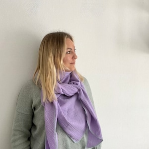 Könnte beinhalten: Eine Frau trägt einen hellgrauen Pullover und eine blaue Jeans mit einem lavendelfarbenen Schal um den Hals.