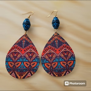 May include: A pair of dangle earrings with a blue and black bead at the top and a teardrop-shaped patterned pendant. The pendant is made of fabric with a geometric design in shades of orange, blue, purple, and pink.