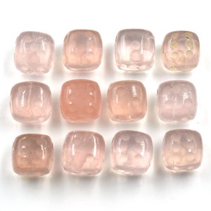 May include: Twelve translucent pink glass beads with a square shape and a raised pattern. The beads are arranged in a grid pattern on a white surface.