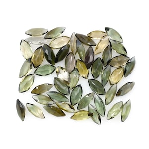 Puede incluir: Una colección de piedras preciosas de forma marquesa verdes y marrones. Las piedras están facetadas y tienen una variedad de tonos de verde y marrón.