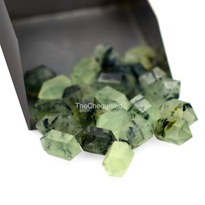 Puede incluir: Primer plano de un montón de puntas de cristal verde y negro. Los cristales son facetados y tienen una apariencia translúcida. Los cristales se derraman de una pala de metal.