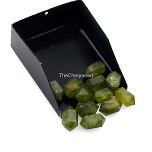 May include: A black metal tray with a pile of green, faceted, gemstone beads. The beads are in various sizes and shapes, and they are all very shiny. The text "TheChequered" is visible on the tray.