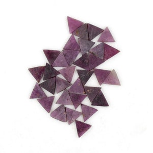 May include: A collection of purple triangular gemstone beads, arranged in a loose, overlapping pattern on a white background.
