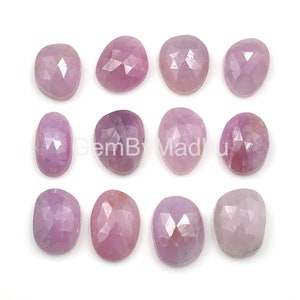 Puede incluir: Doce piedras preciosas ovaladas facetadas de color rosa. Las piedras preciosas están dispuestas en tres filas de cuatro.