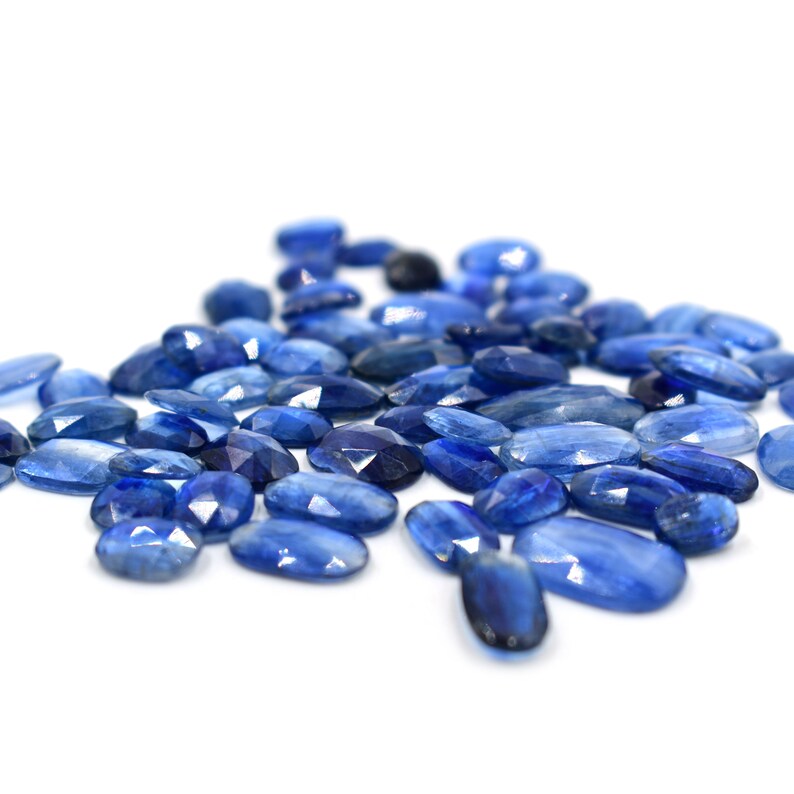 May include: A collection of oval-shaped blue kyanite gemstones. The stones are faceted and have a light blue color with a slight shimmer.