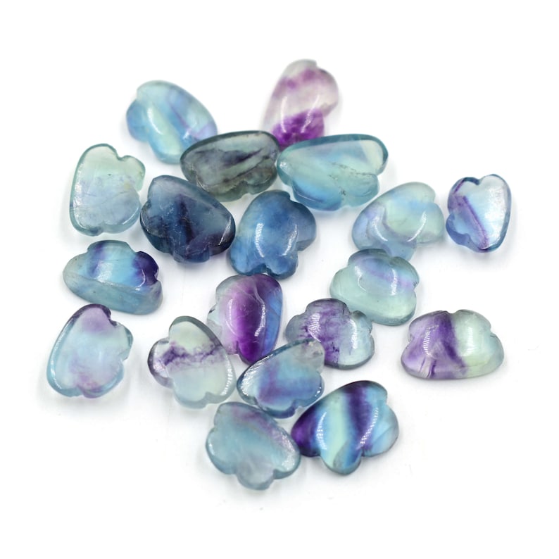 Op de afbeelding: Een verzameling van 18 blauwe, groene en paarse fluorite kralen in de vorm van een wolk. De kralen zijn glad en gepolijst.