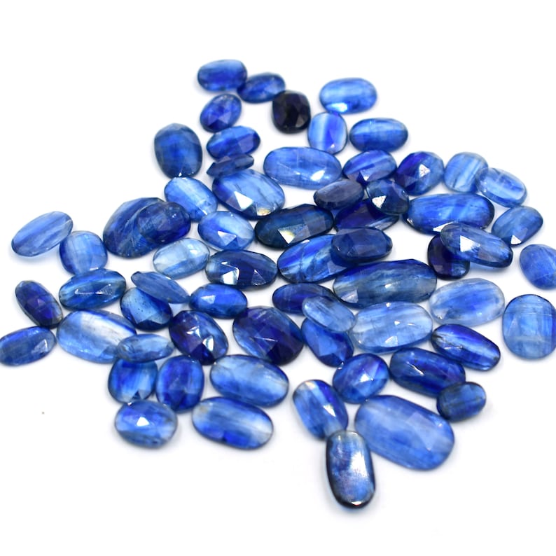 May include: A collection of blue kyanite gemstones, each with a unique, faceted oval shape. The stones have a light blue color with a slight shimmer.