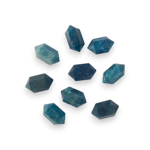 May include: A collection of eight blue-green crystal points, each with a faceted, elongated shape. The crystals vary in shades of blue and green, with some appearing more translucent than others. They are arranged on a white background.